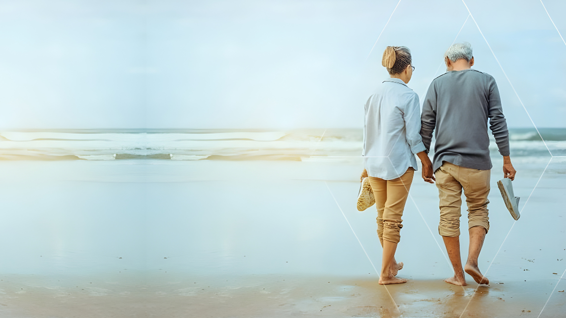 A senior couple walking along the shore, symbolizing the leisure and security achieved through long-term wealth preservation.