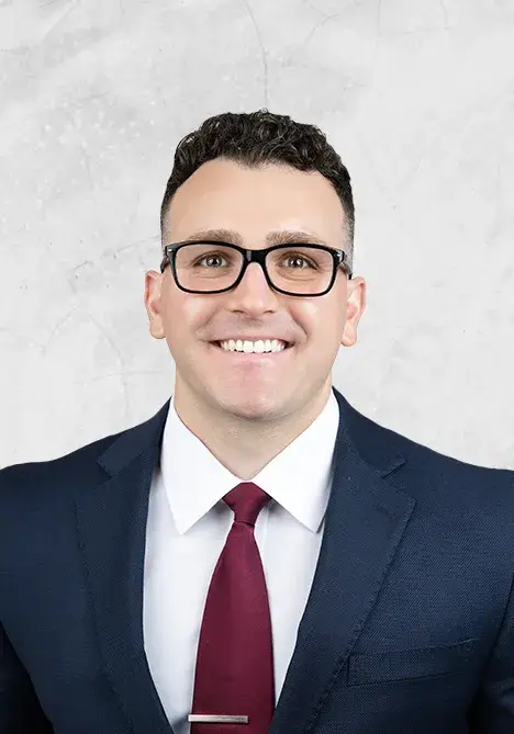 Professional headshot: man in a navy suit, white shirt, burgundy tie, wearing glasses, smiling against a light gray background.