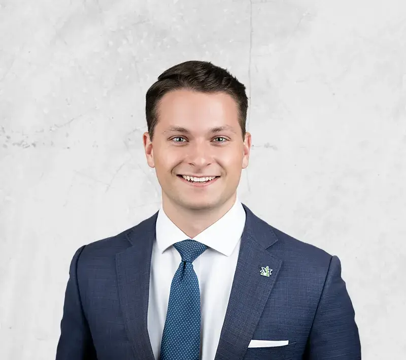Head-and-shoulders portrait of a smiling man in a navy suit, white shirt, and blue tie against a light gray backdrop.
