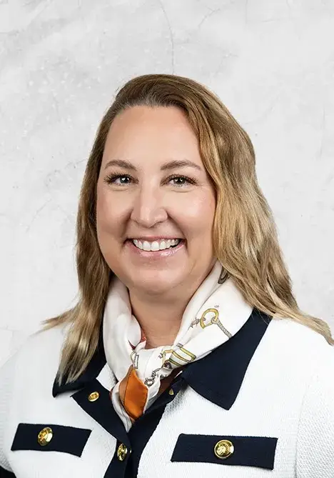 Portrait of a smiling professional woman with shoulder-length blonde hair, wearing a white blazer with dark trim and a patterned scarf.