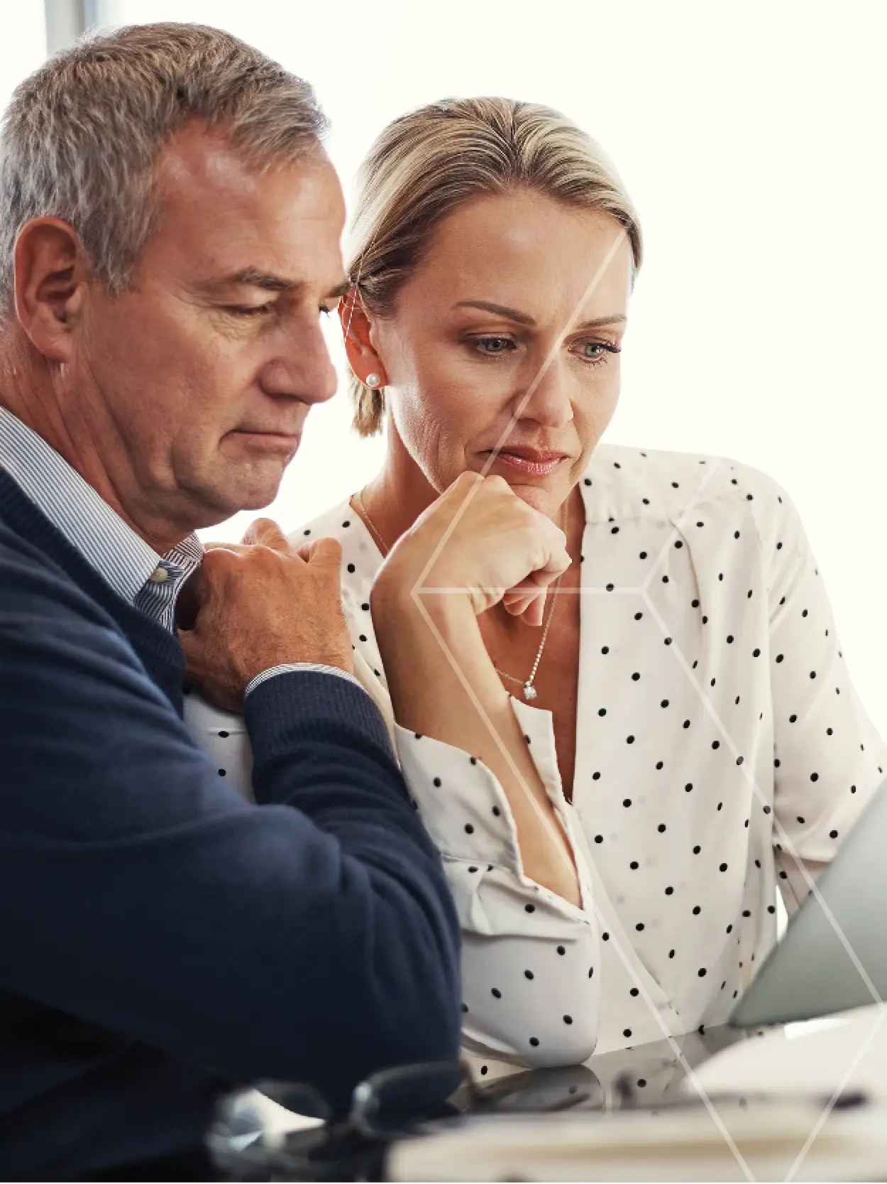 Two colleagues—the man on the left and woman on the right—lean in to review something on a laptop screen together, looking focused and thoughtful.