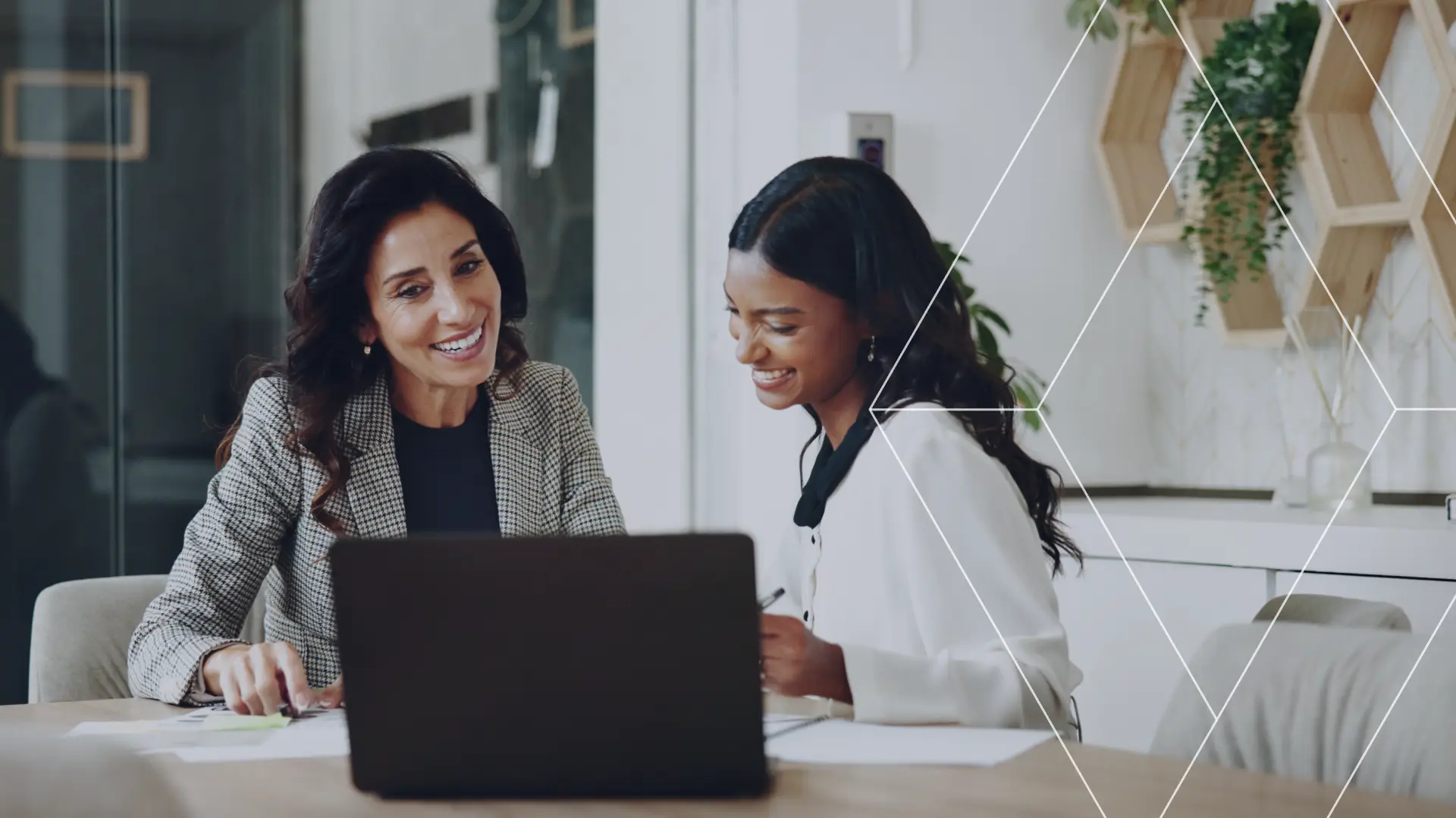 Two businesswomen smiling while reviewing information together on a laptop in an office.